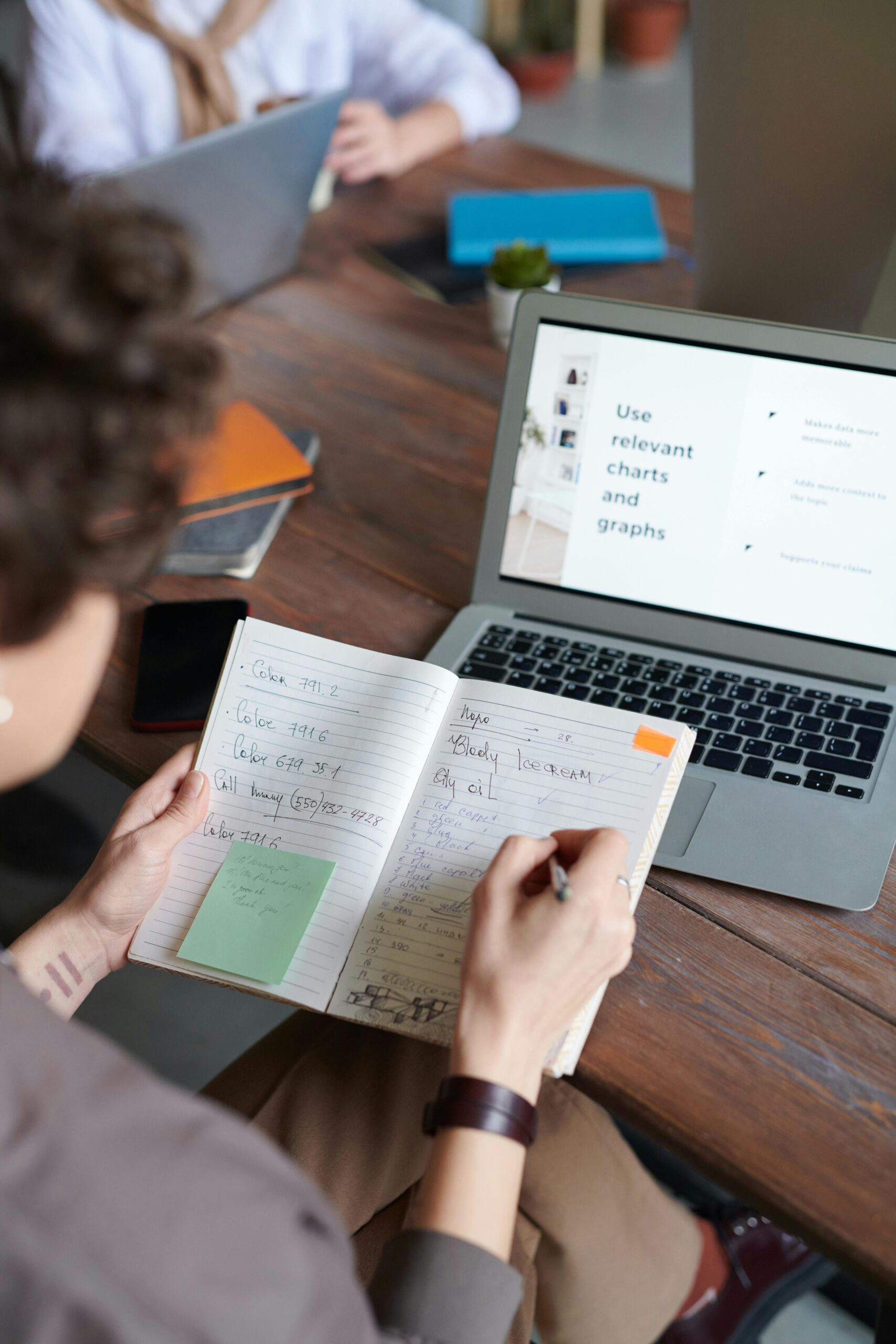 Individual writing notes at a laptop with a digital chart presentation indoors.
